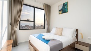 A hotel room with a bed, a nightstand, a window with curtains, a city view, and a painting on the wall. - HAYA SOHO SAIGON (Ho Chi Minh City)