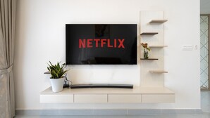 A modern living room with a flat-screen TV mounted on a wall, a potted plant, and a minimalist shelving unit. - HAYA SOHO SAIGON (Ho Chi Minh City)