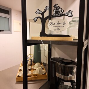 Una cocina con cafetera, una bandeja de tazas y un letrero decorativo con un árbol y una taza de café.