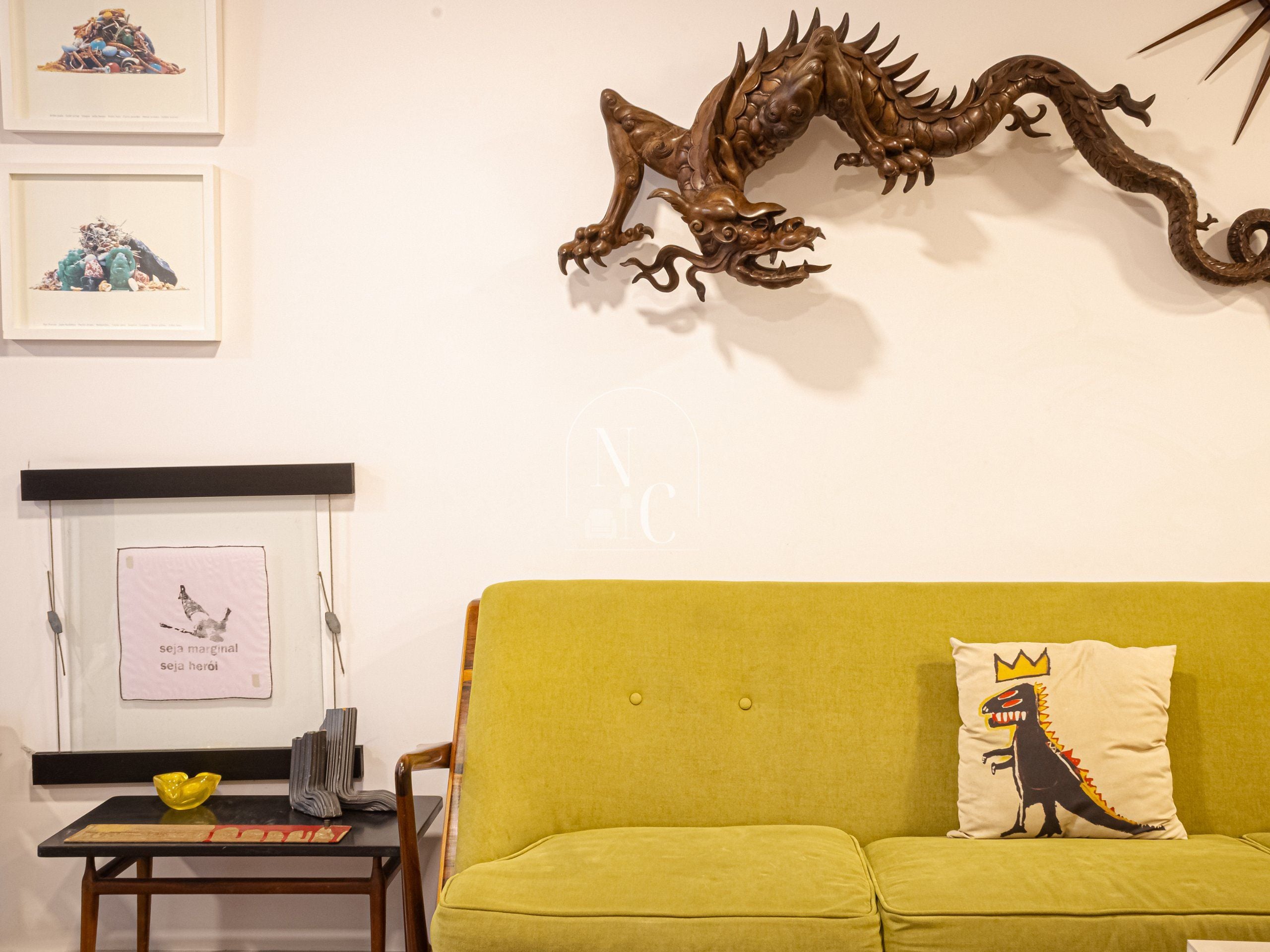 A room with a green sofa, a framed picture, a decorative dragon, and a small table with a yellow bowl.