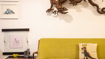 A room with a green sofa, a framed picture, a decorative dragon, and a small table with a yellow bowl.