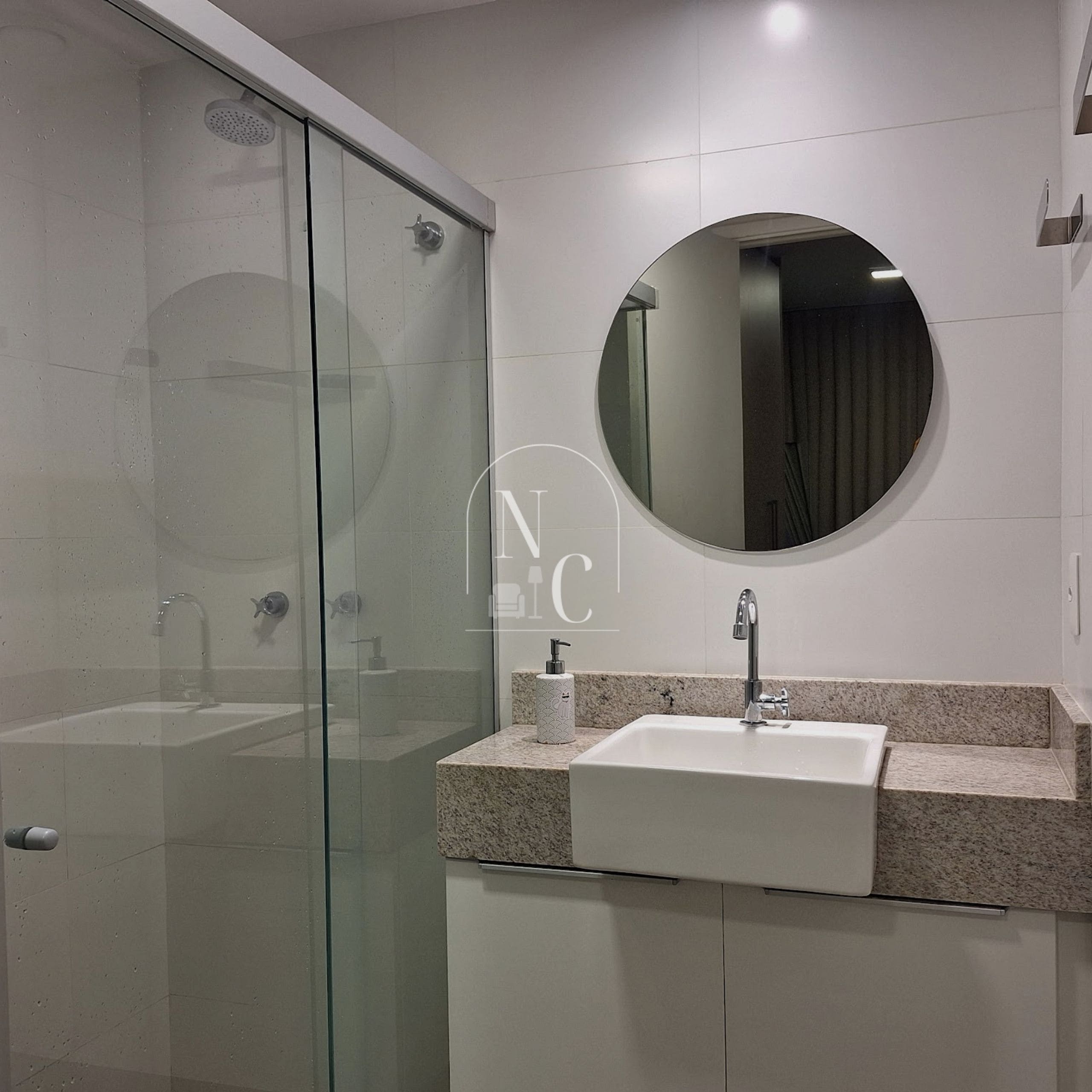 A modern bathroom with a glass shower enclosure, a round mirror, and a granite countertop sink.