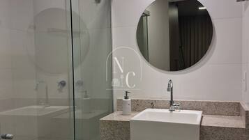 A modern bathroom with a glass shower enclosure, a round mirror, and a granite countertop sink.