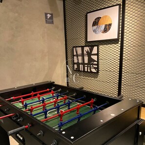 Une table de baby-foot dans une pièce dont le mur est texturé et au-dessus de laquelle est accrochée une œuvre d’art encadrée.