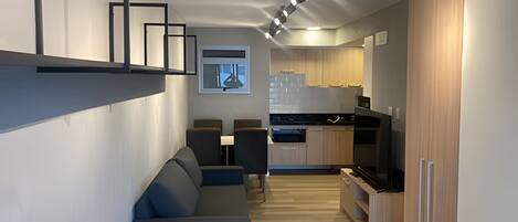Una cocina moderna con armarios de madera, horno empotrado y una zona de comedor con sofá azul.