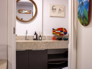 Un baño con encimera de granito, un espejo, un lavamanos, dispensador de jabón, portalápices para cepillos de dientes y un jabonero decorativo con forma de pez.