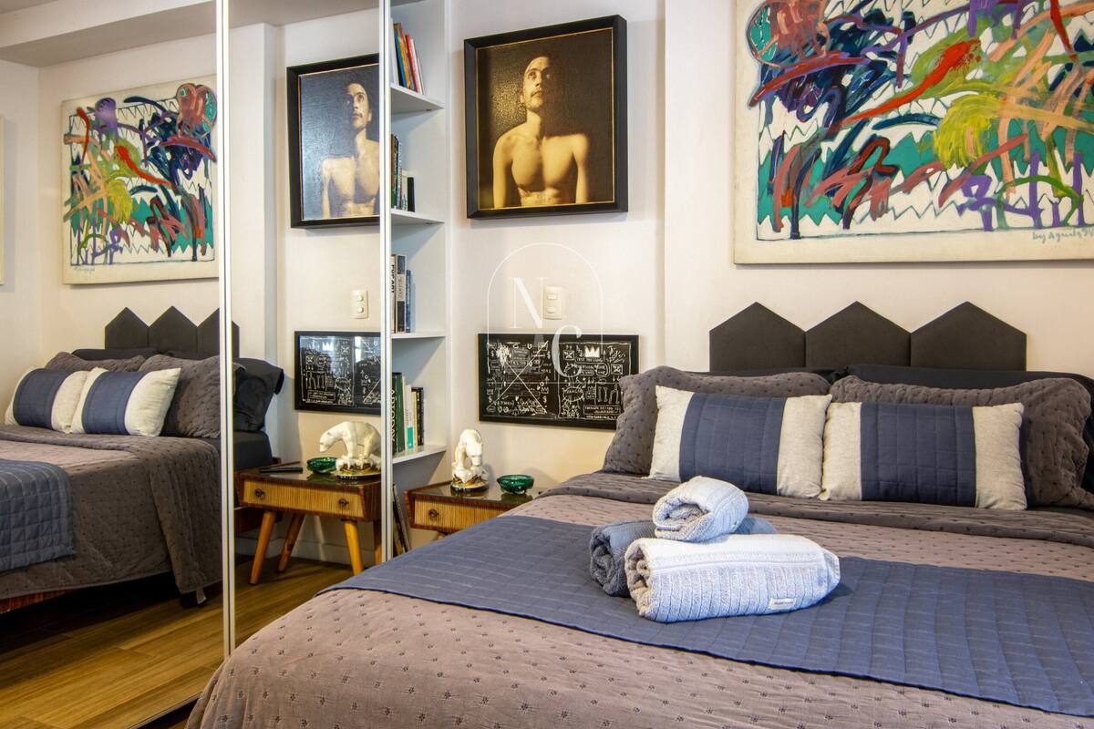 Quarto com duas camas, obras de arte nas paredes e uma estante de livros.