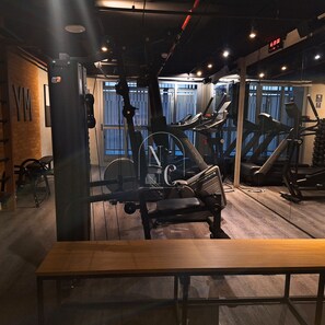 Une salle de sport équipée de matériel d’exercice, d’un banc en bois et d’un mur recouvert de miroirs.