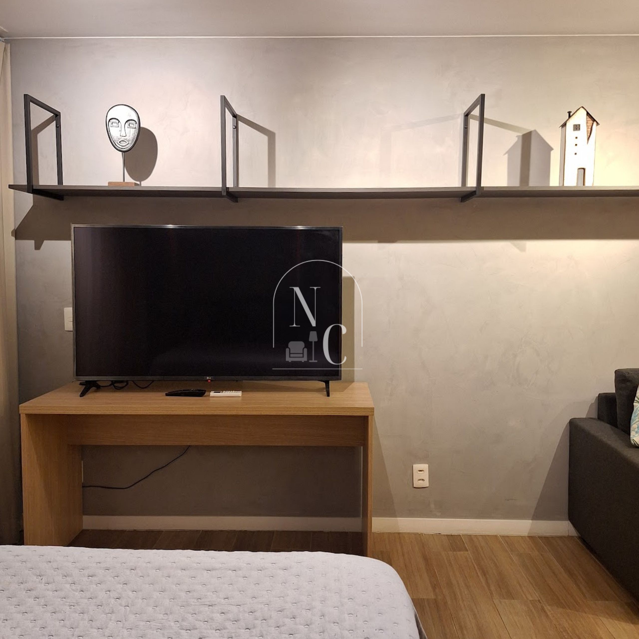 A modern room with a large flat-screen TV on a wooden stand, a bed with a white duvet, and a small sofa.