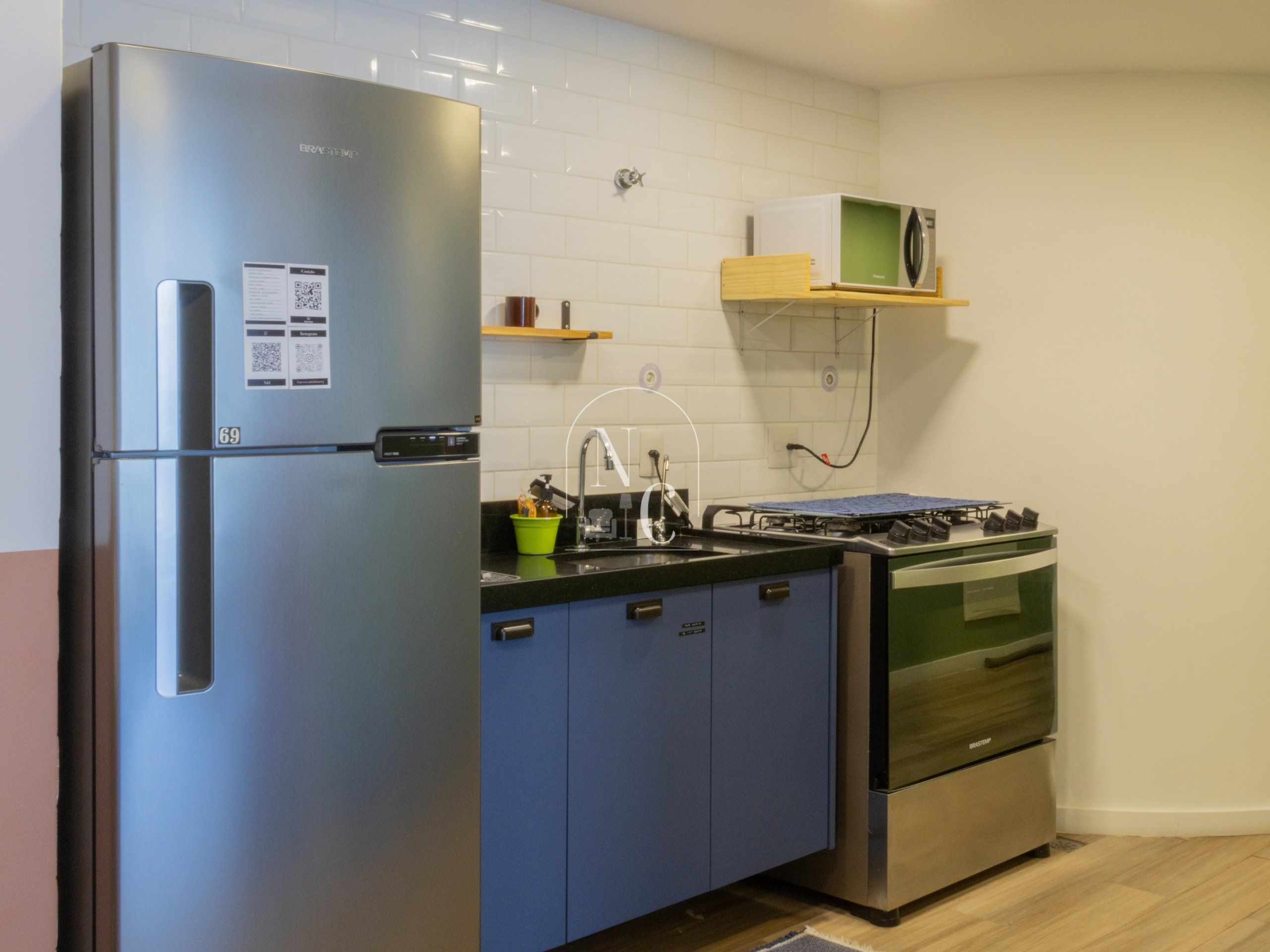 Een functionele keuken met een koelkast van roestvrij staal, een magnetron, een fornuis en een spoelbak.