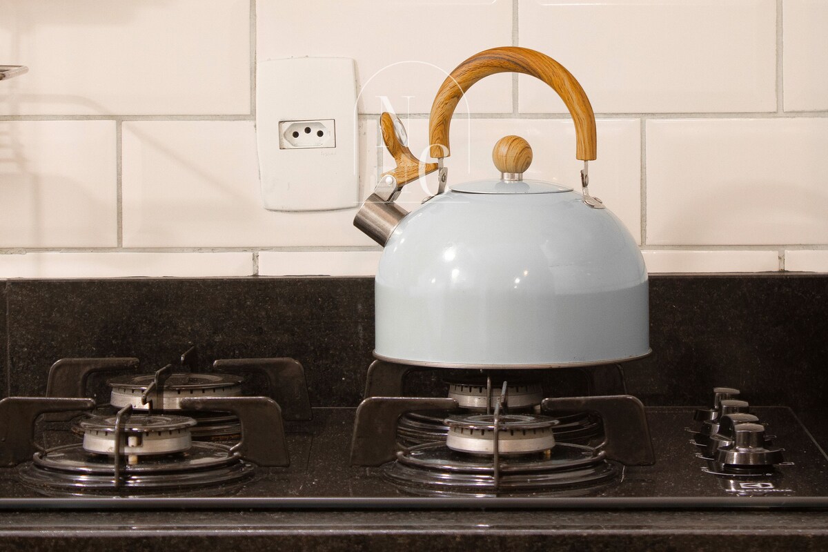 Una cocina con estufa a gas, hervidor y salpicadero de azulejos blancos.