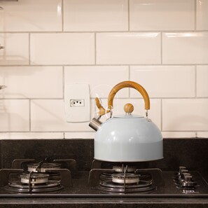 Una cocina con estufa a gas, hervidor y salpicadero de azulejos blancos.