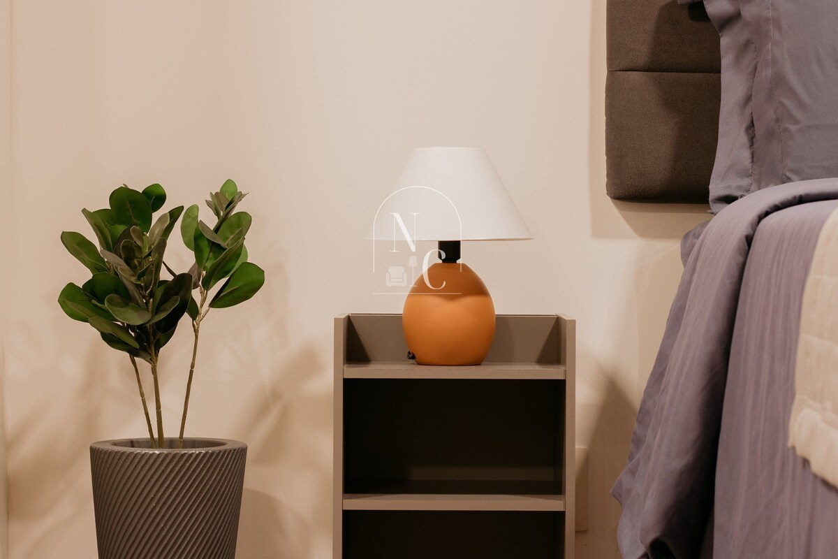 Una habitación ordenada con una planta en maceta, una lámpara en un estante y una cama con una colcha.
