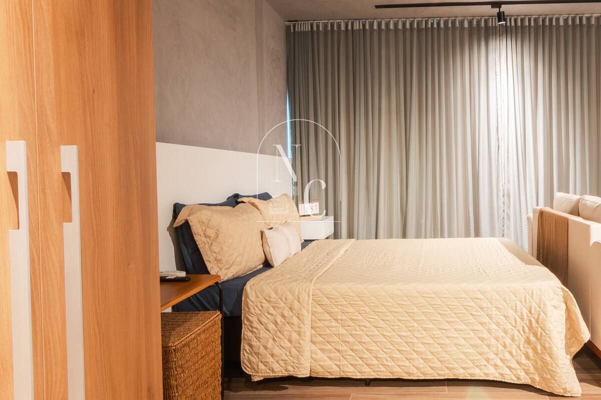 Quarto moderno com uma cama grande, uma mesa de cabeceira, uma luminária e vista para o exterior através de cortinas.