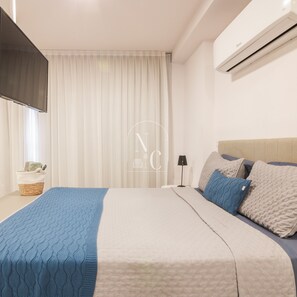 A bedroom with a bed, a bedside table, a lamp, a wall-mounted air conditioner, and a window with curtains. - RioDowntown Hub by RNC Flats (Rio de Janeiro)