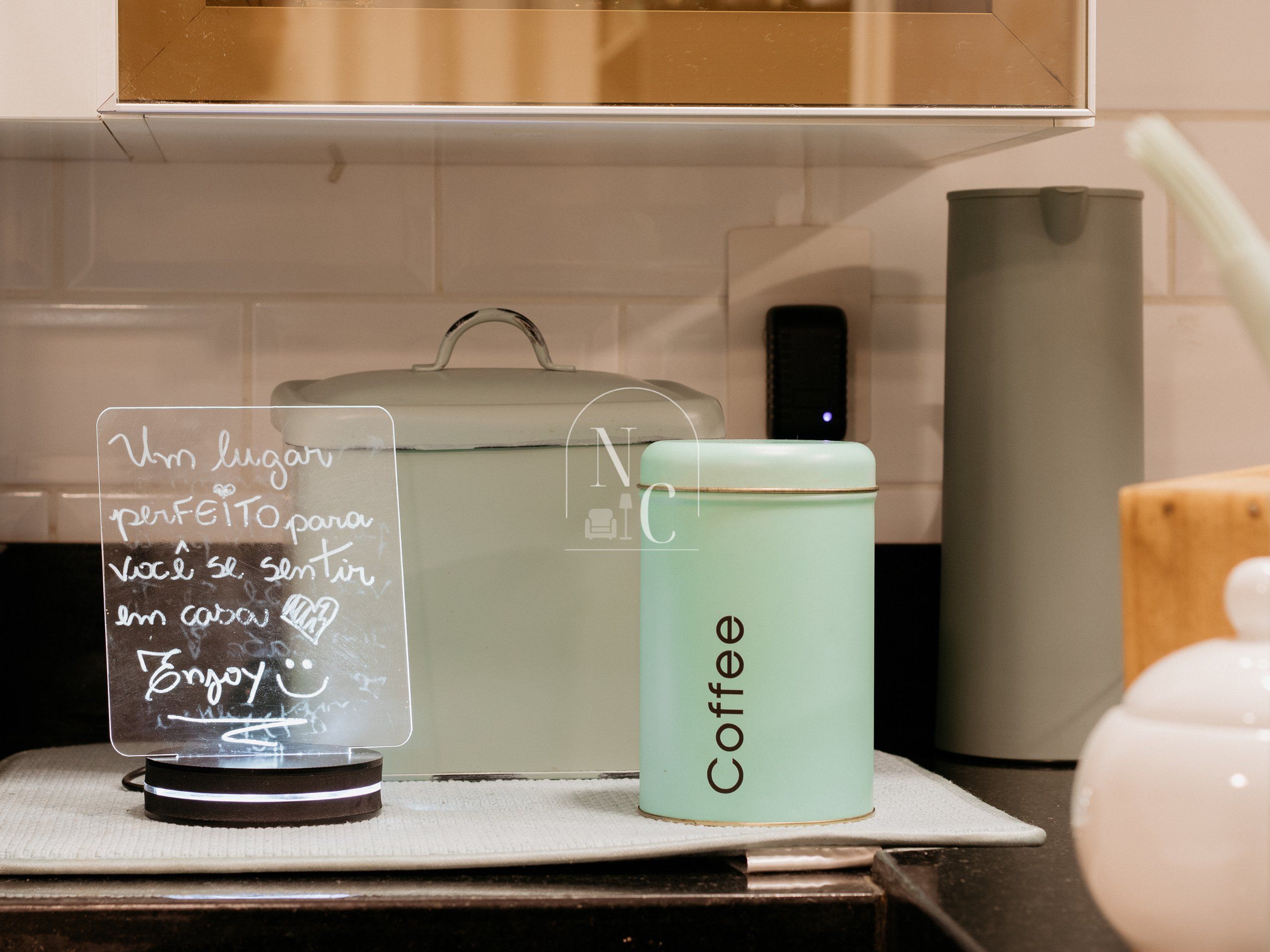 A kitchen counter with a coffee container, a glass jar with a handwritten note, and a white appliance in the background.