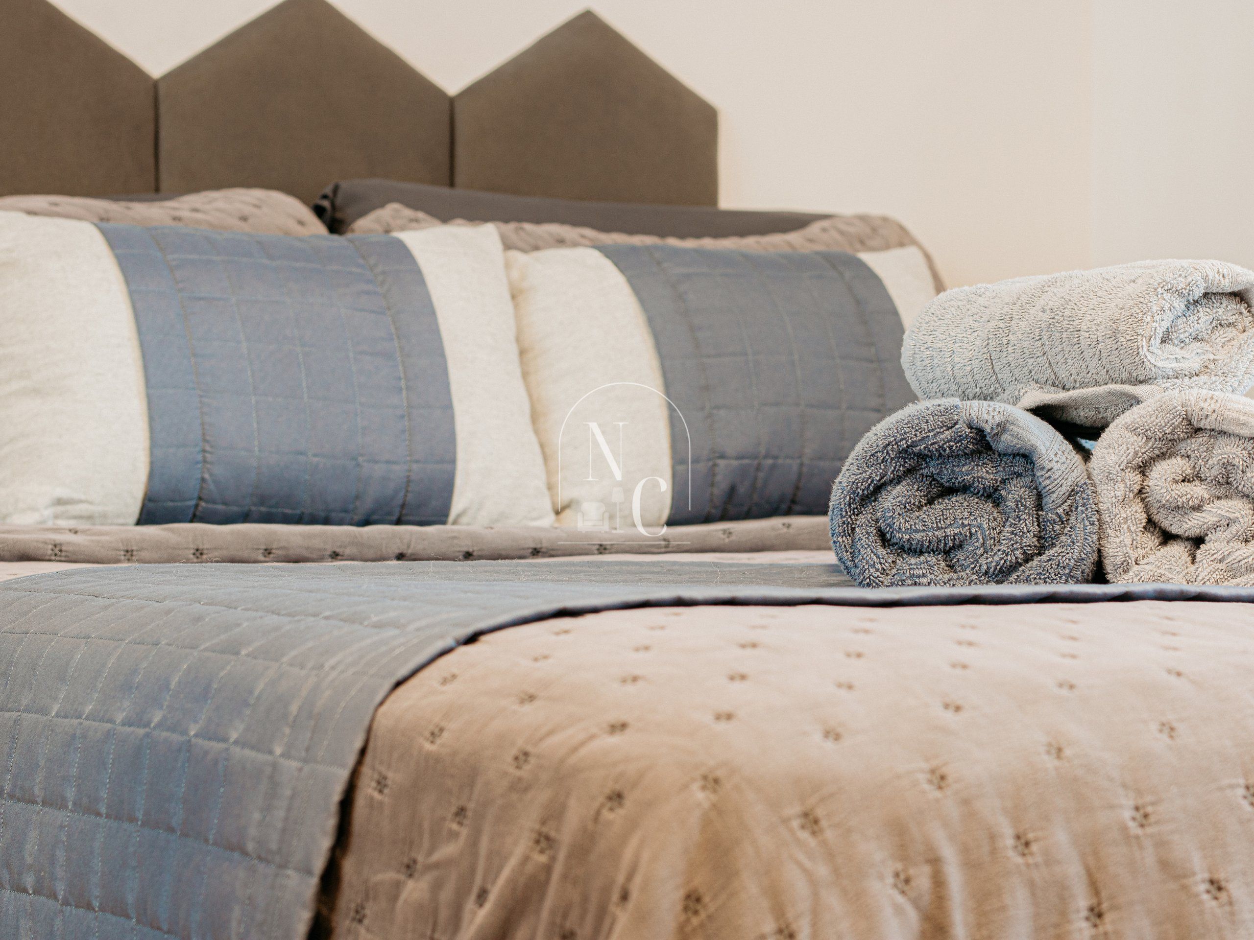 A neatly made bed with a quilted bedspread, pillows, and rolled towels.