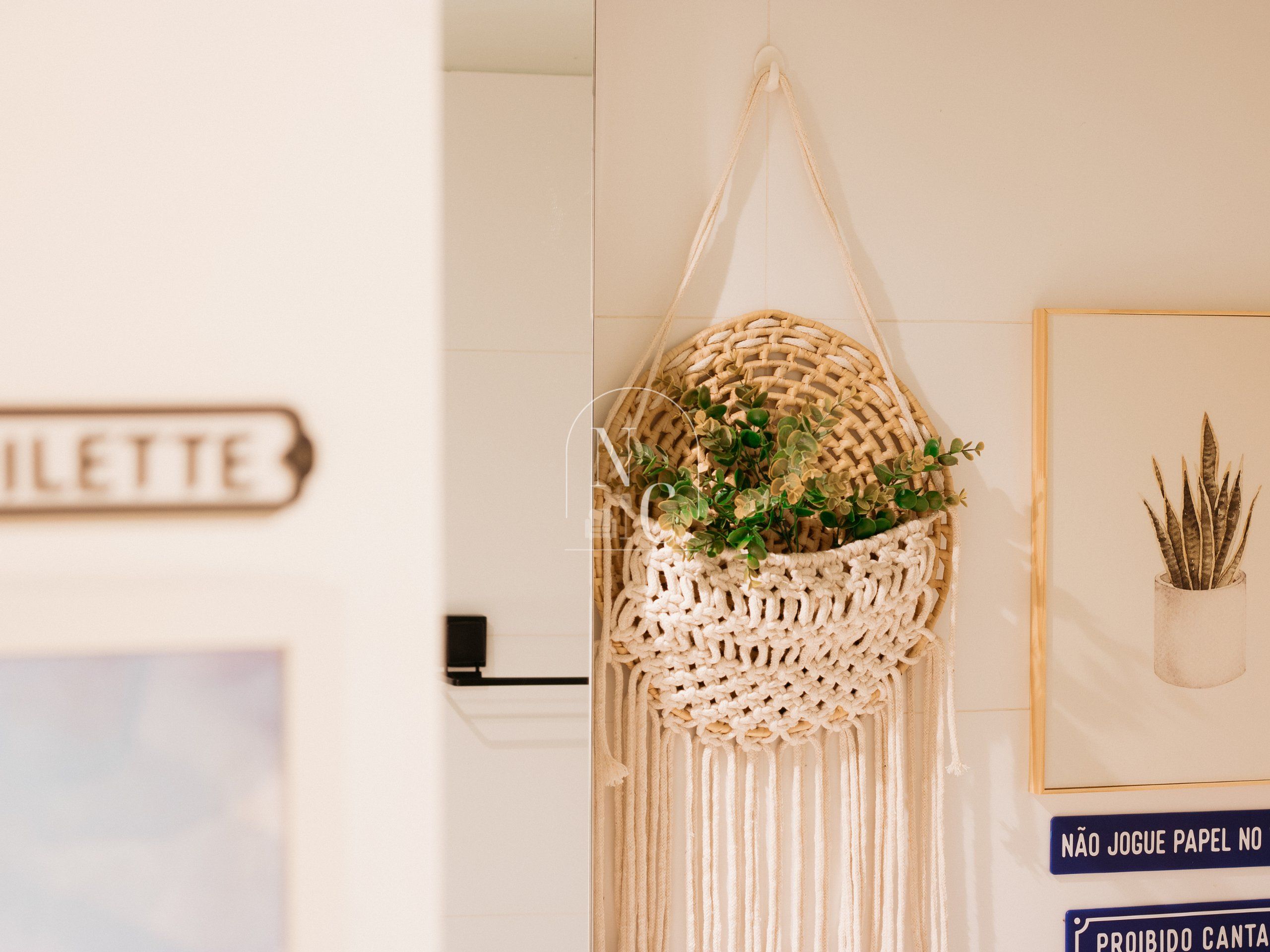 A macrame wall hanging with greenery, a framed plant, and a sign with text.