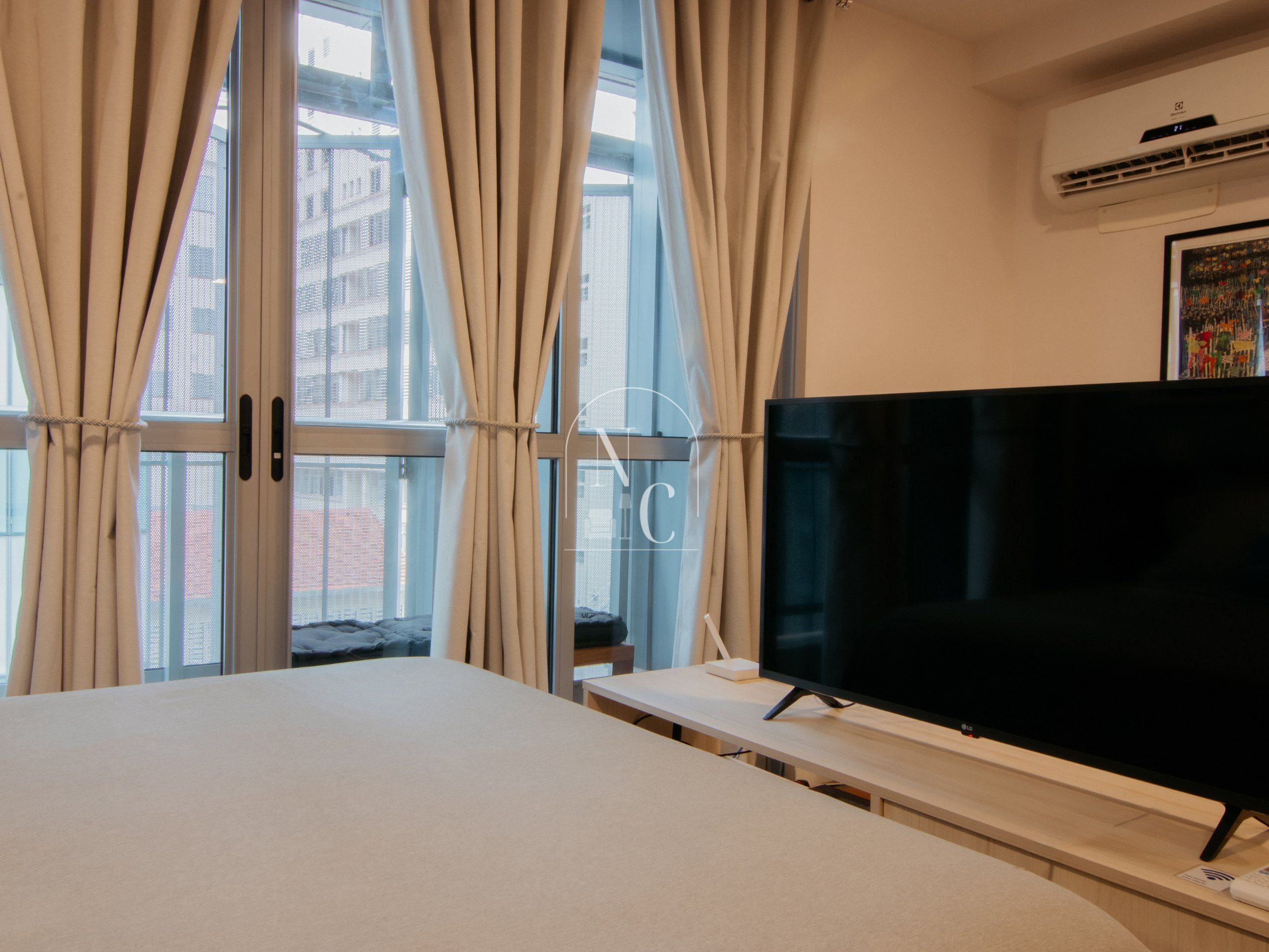 A room with a bed, a TV on a stand, and a window with curtains.