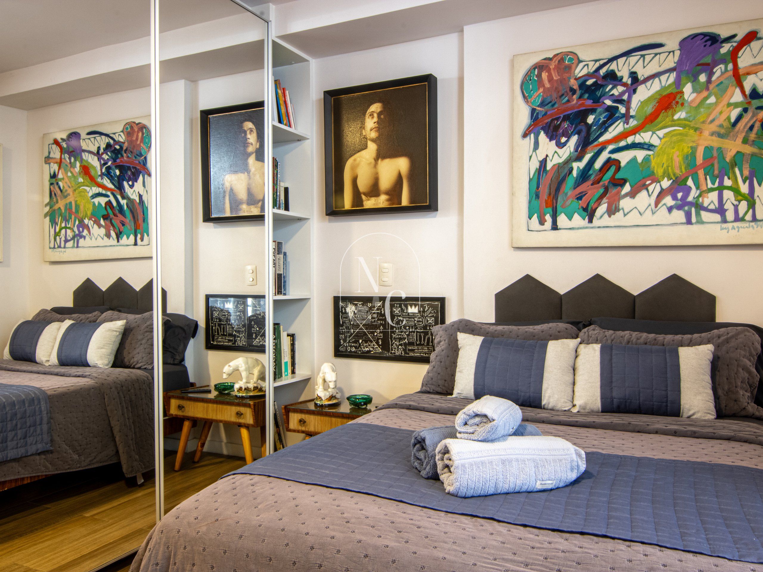 Ein Schlafzimmer mit zwei Betten, Bildern an den Wänden und einem Bücherregal.