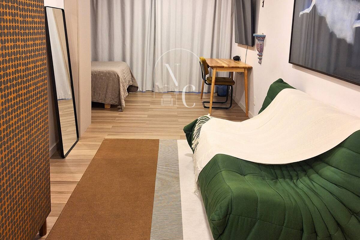 Quarto de hotel com cama, escrivaninha, poltrona, televisão e um quadro na parede.