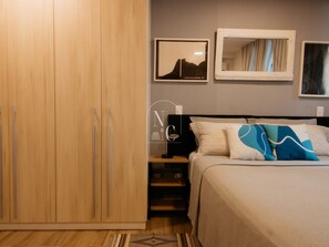 Un dormitorio con cama, armario, mesita de noche, lámpara y dos cuadros en la pared.