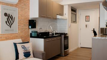 Een moderne keuken met een ingebouwde oven, een kookplaat en een spoelbak. Er is een bakstenen muur, een kunstwerk in een lijst en een bank met kussens.