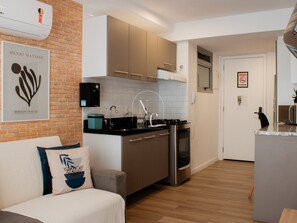 Eine moderne Küche mit integriertem Backofen, Herd und Spüle. Eine Ziegelwand, ein gerahmtes Kunstwerk und eine Couch mit Kissen sind ebenfalls vorhanden.