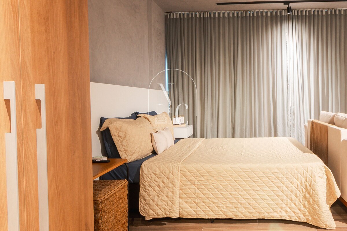 Un dormitorio moderno con una cama grande, una mesita de noche, una lámpara y vistas al exterior a través de cortinas.