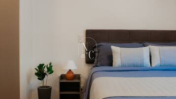 A bedroom with a bed, bedside table, lamp, and a potted plant.