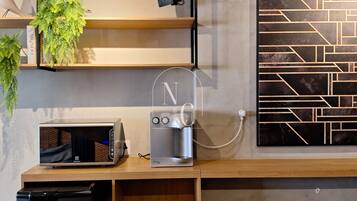 A kitchenette with a microwave, coffee maker, and a small refrigerator. There are shelves with plants and a wall-mounted light.