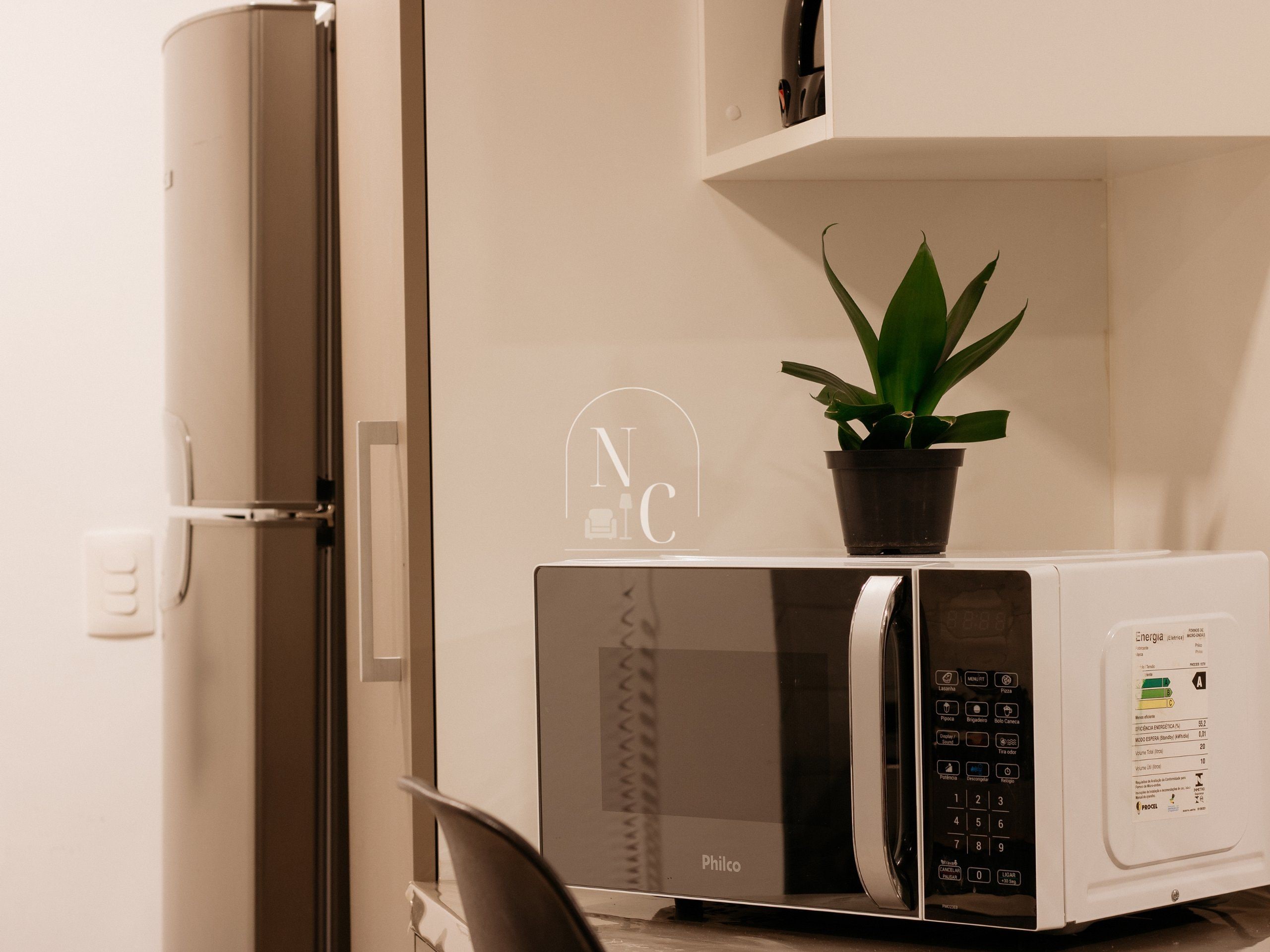 A kitchen with a microwave, a refrigerator, and a potted plant on the counter.
