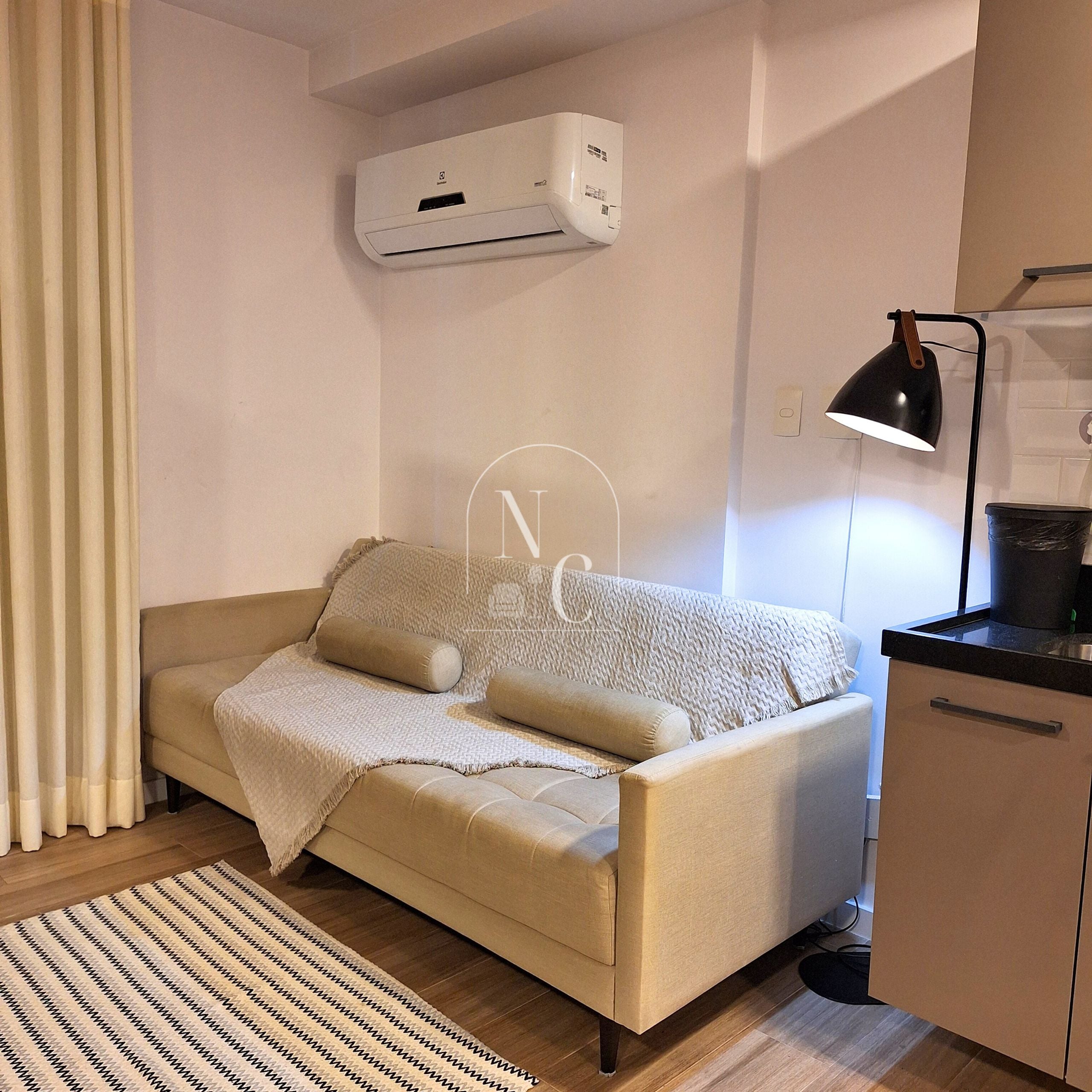 A modern living room with a sofa, a small kitchen area, and a wall-mounted air conditioner.