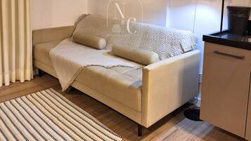 A modern living room with a sofa, a small kitchen area, and a wall-mounted air conditioner.