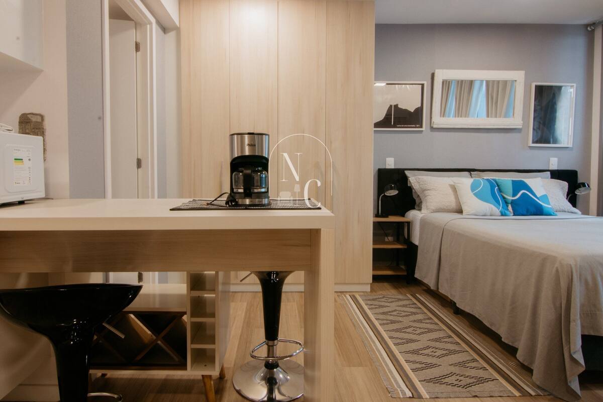Quarto de hotel com uma cama, cafeteira, escrivaninha e uma cadeira.
