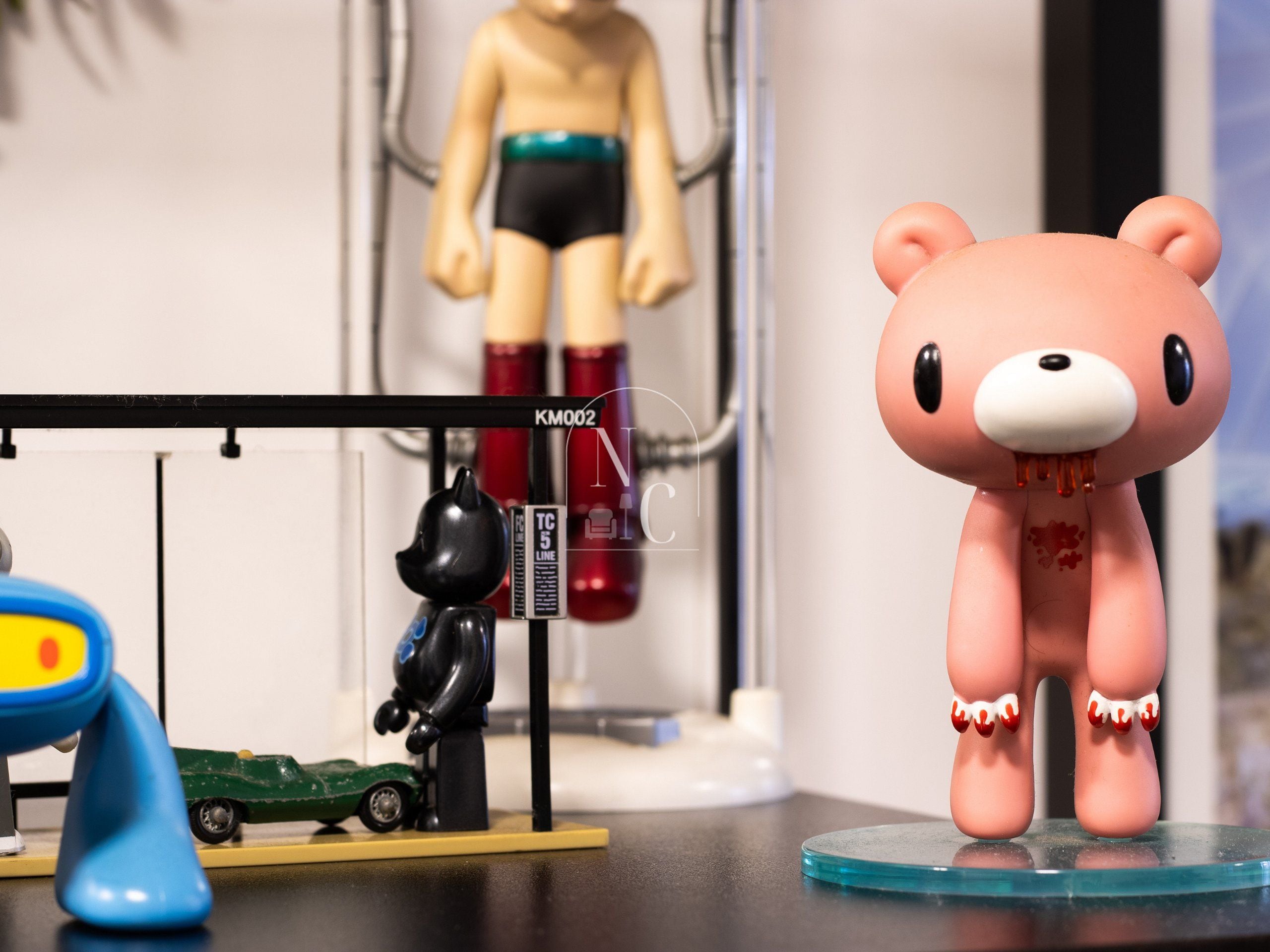 Una figura de oso sobre una base de vidrio transparente, un pequeño coche de juguete verde y una figura de juguete negra sobre un pedestal negro.