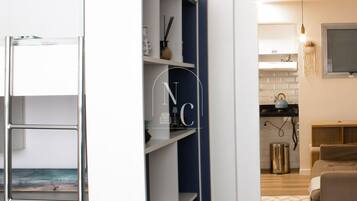 Un interior moderno con un armario blanco y azul a rayas, una zona de cocina con hervidor y una sala de estar con sofá.