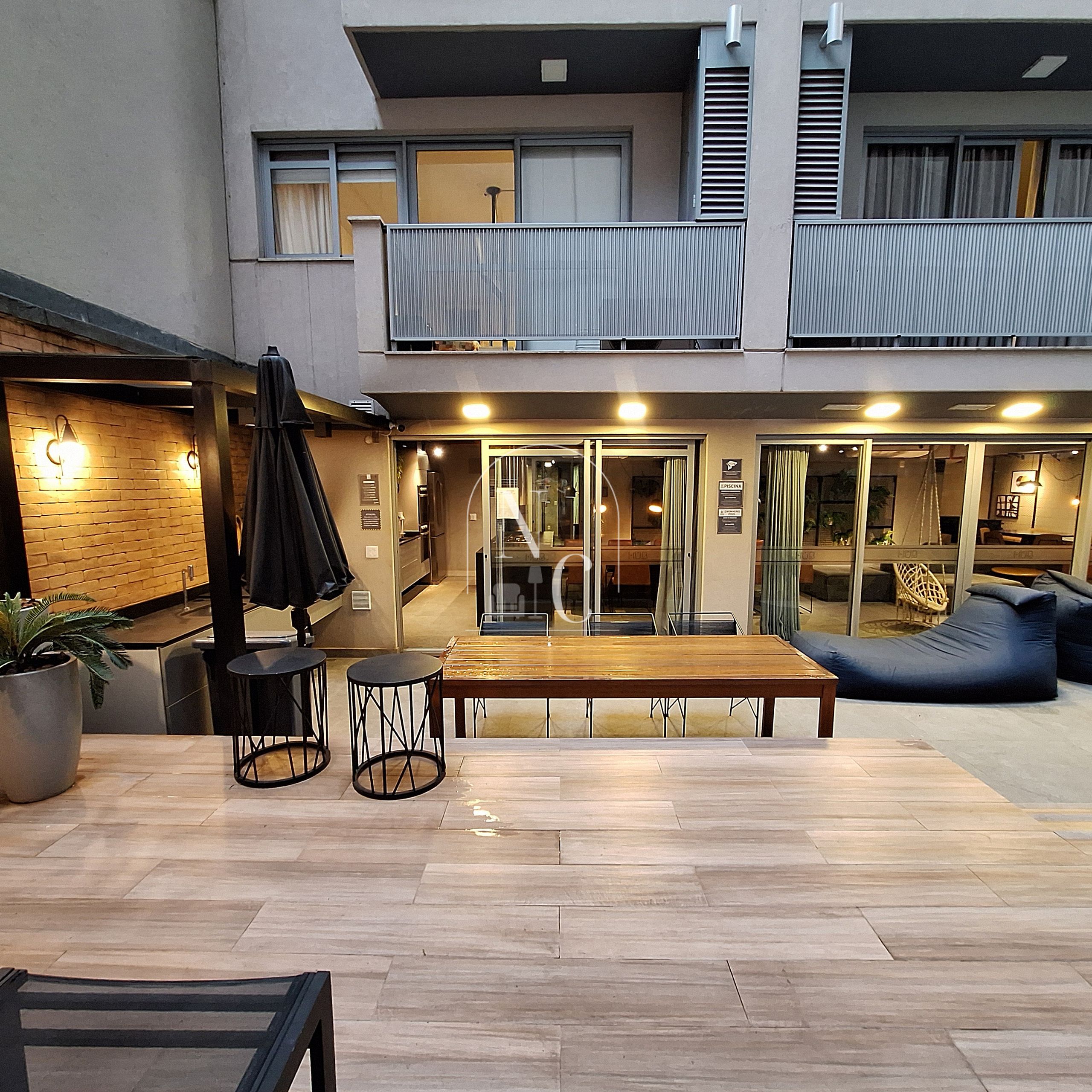 A modern outdoor seating area with a wooden table and chairs, a potted plant, and a glass door entrance.
