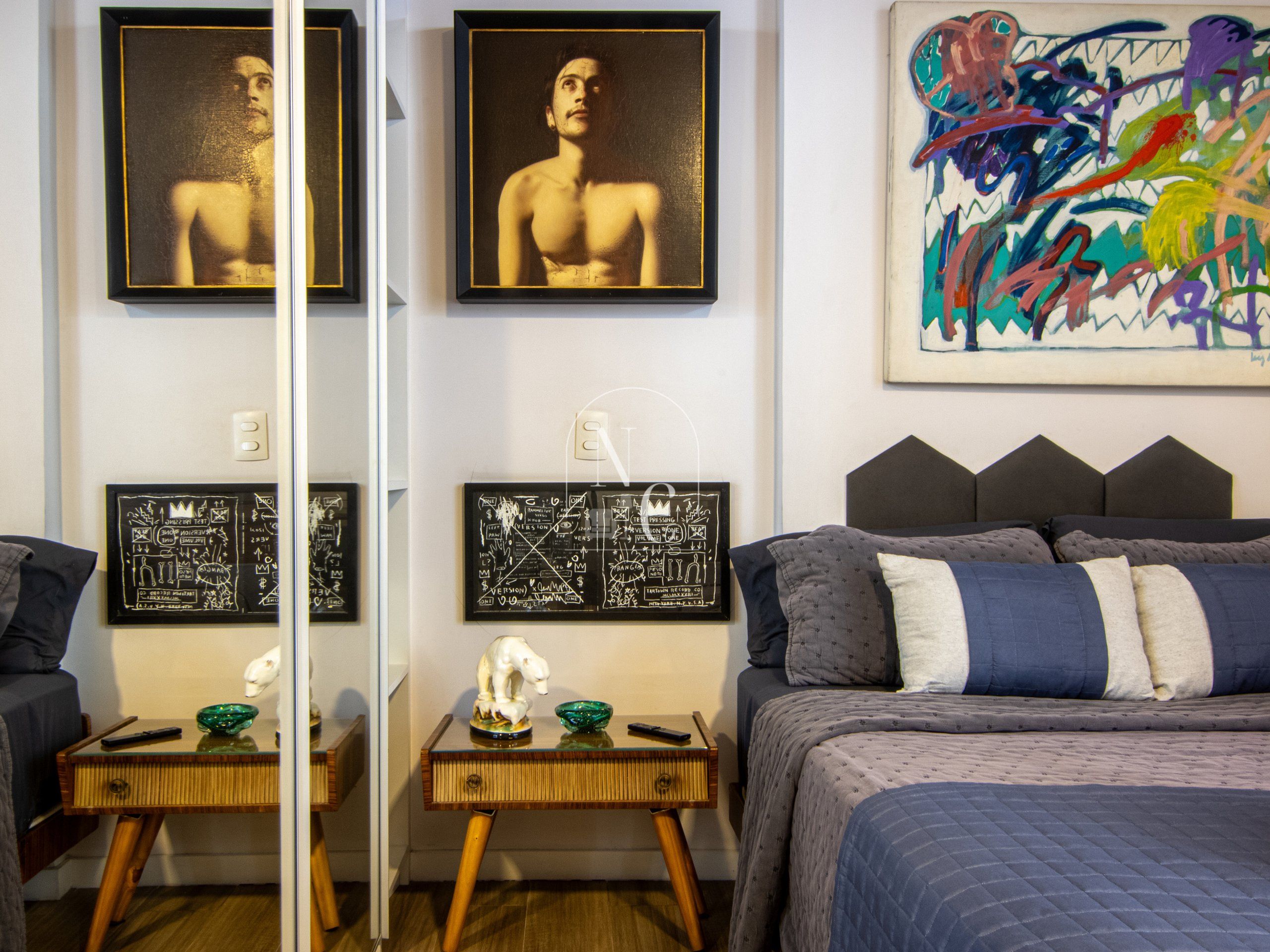 A bedroom with a bed, a nightstand, a mirror, and artwork on the walls.