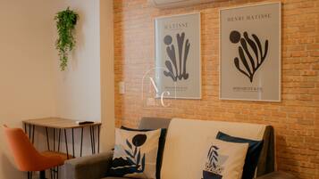 Una habitación con pared de ladrillo, un sofá gris con cojines decorativos, una mesita y un equipo de aire acondicionado.