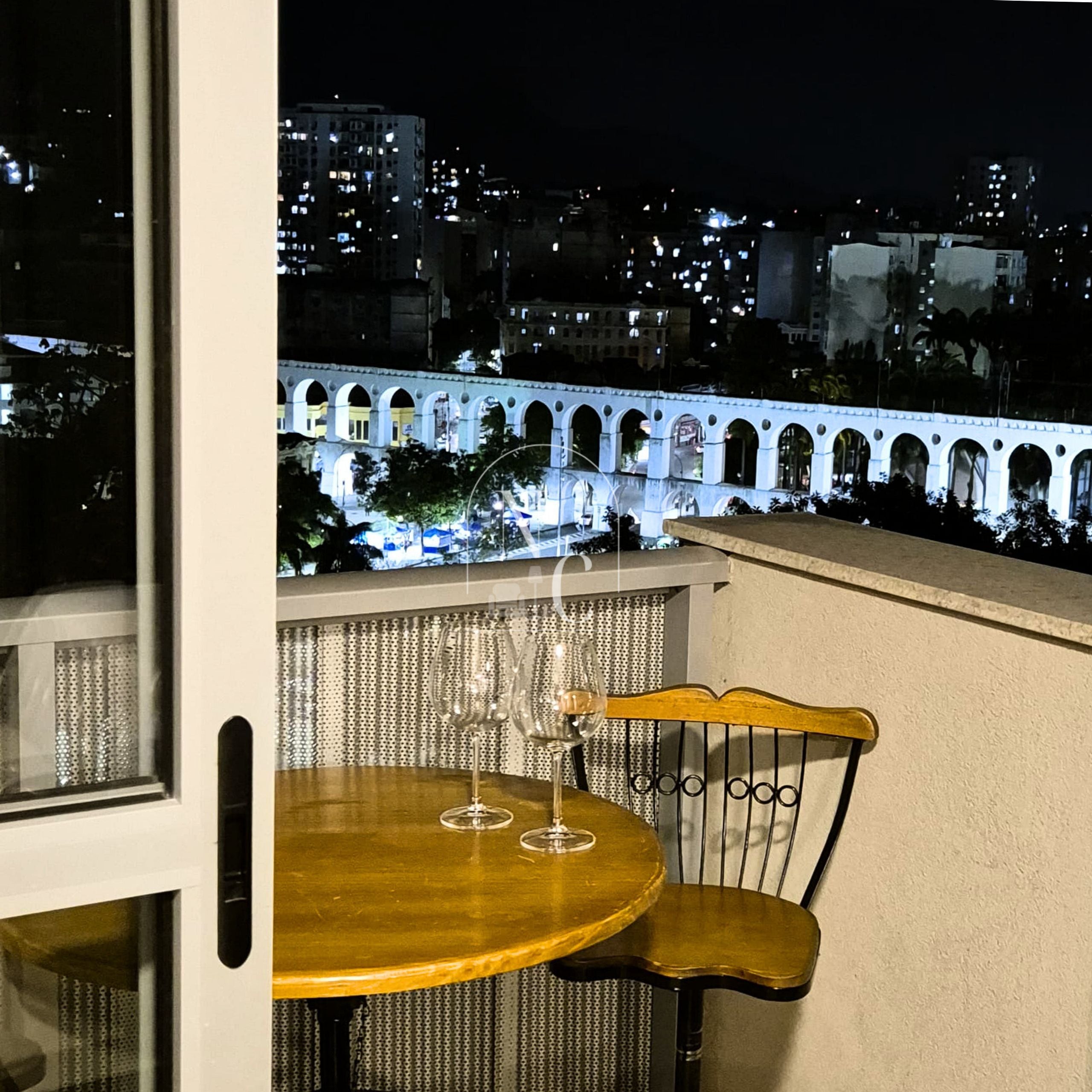 Un balcon avec une table et une chaise, donnant sur une vue panoramique de la ville la nuit.