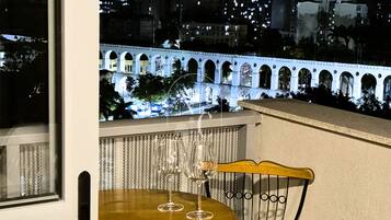 Un balcon avec une table et une chaise, donnant sur une vue panoramique de la ville la nuit.