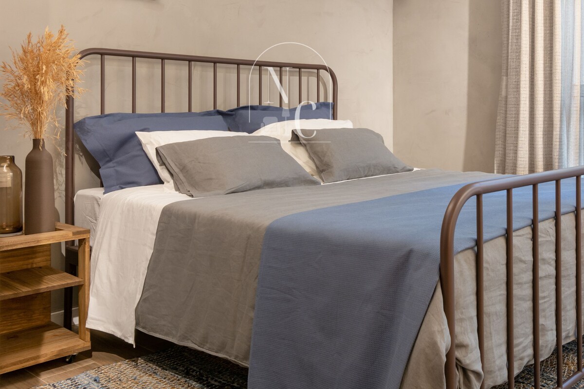 Un dormitorio con cama, mesita de noche, lámpara, unidad de aire acondicionado y un cuadro en la pared.