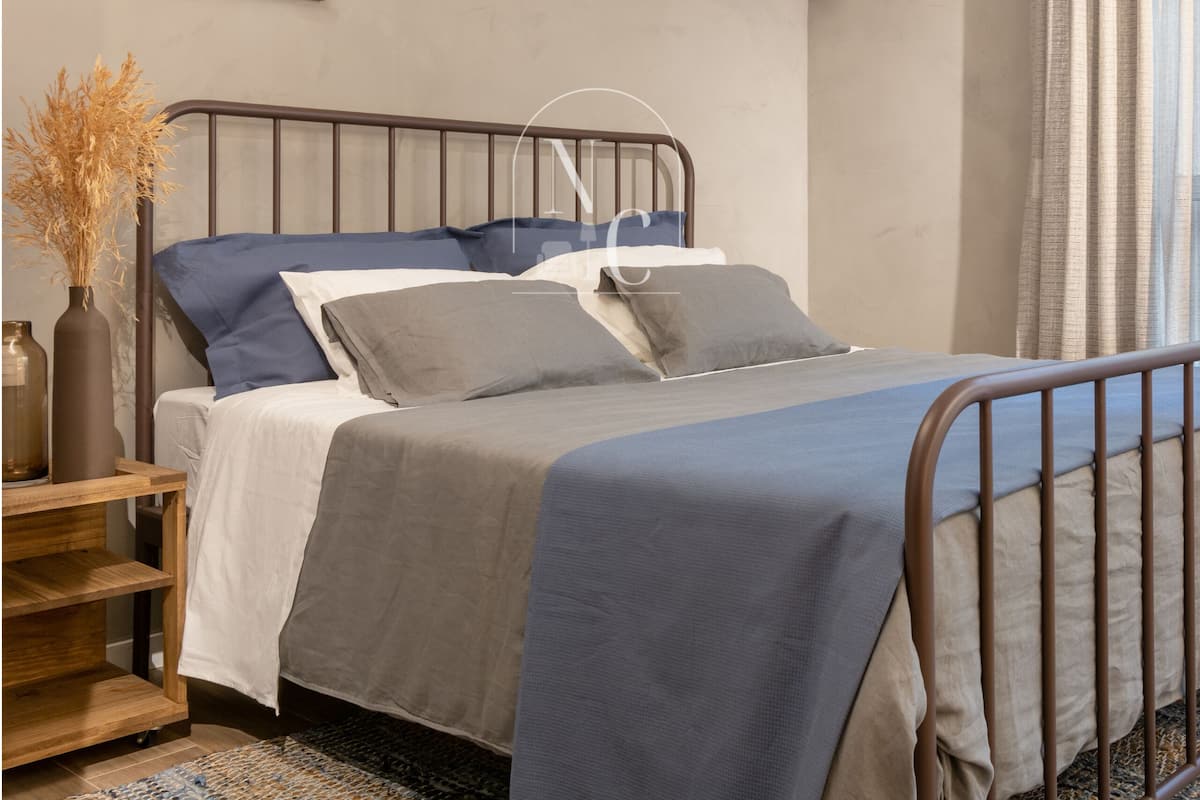 Quarto com cama, mesa de cabeceira, abajur, ar condicionado e um quadro na parede.
