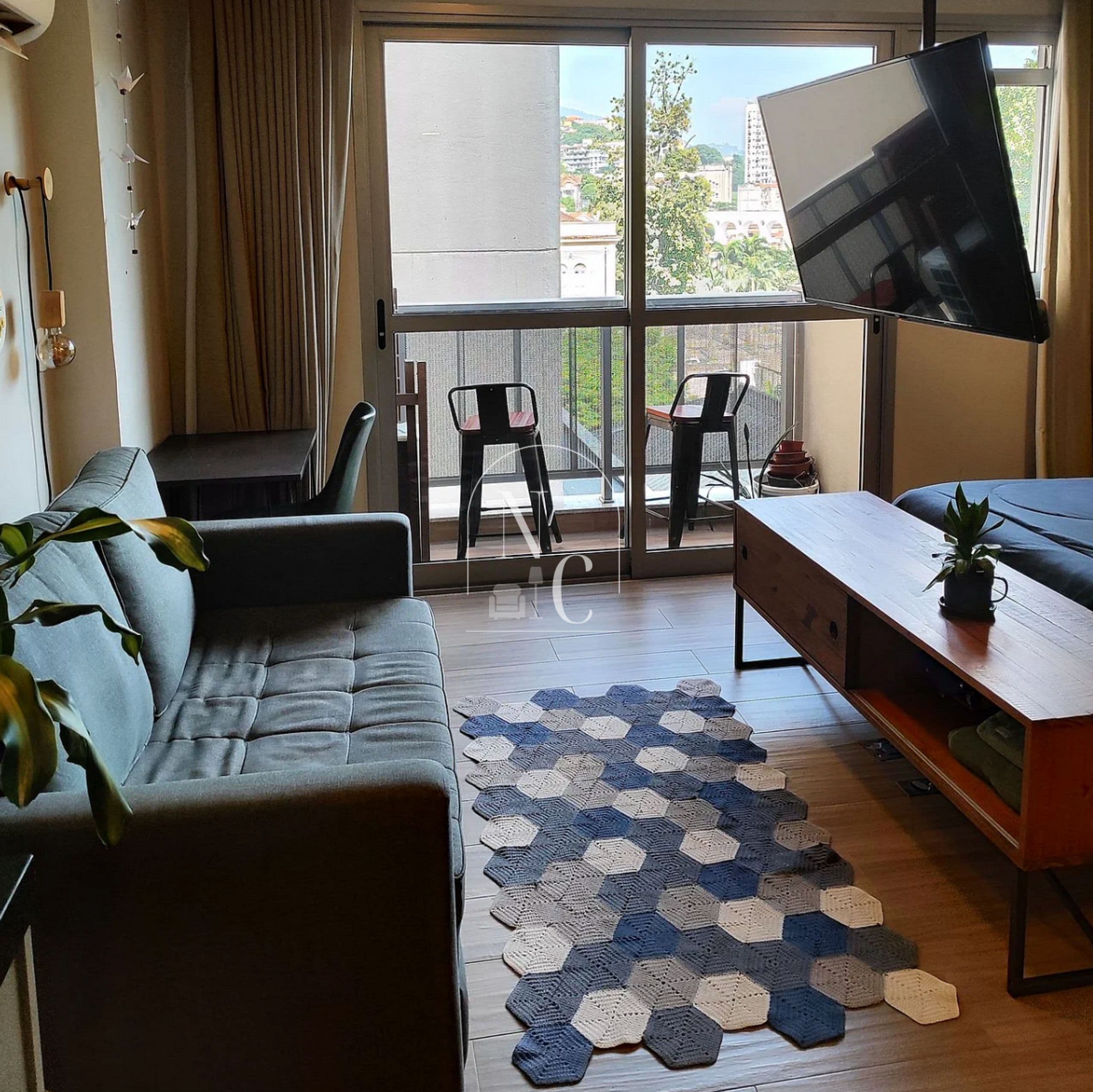 Ein Wohnzimmer mit einer Couch, Sesseln, einem Fernseher, einem Holztisch und Blick durch große Fenster.