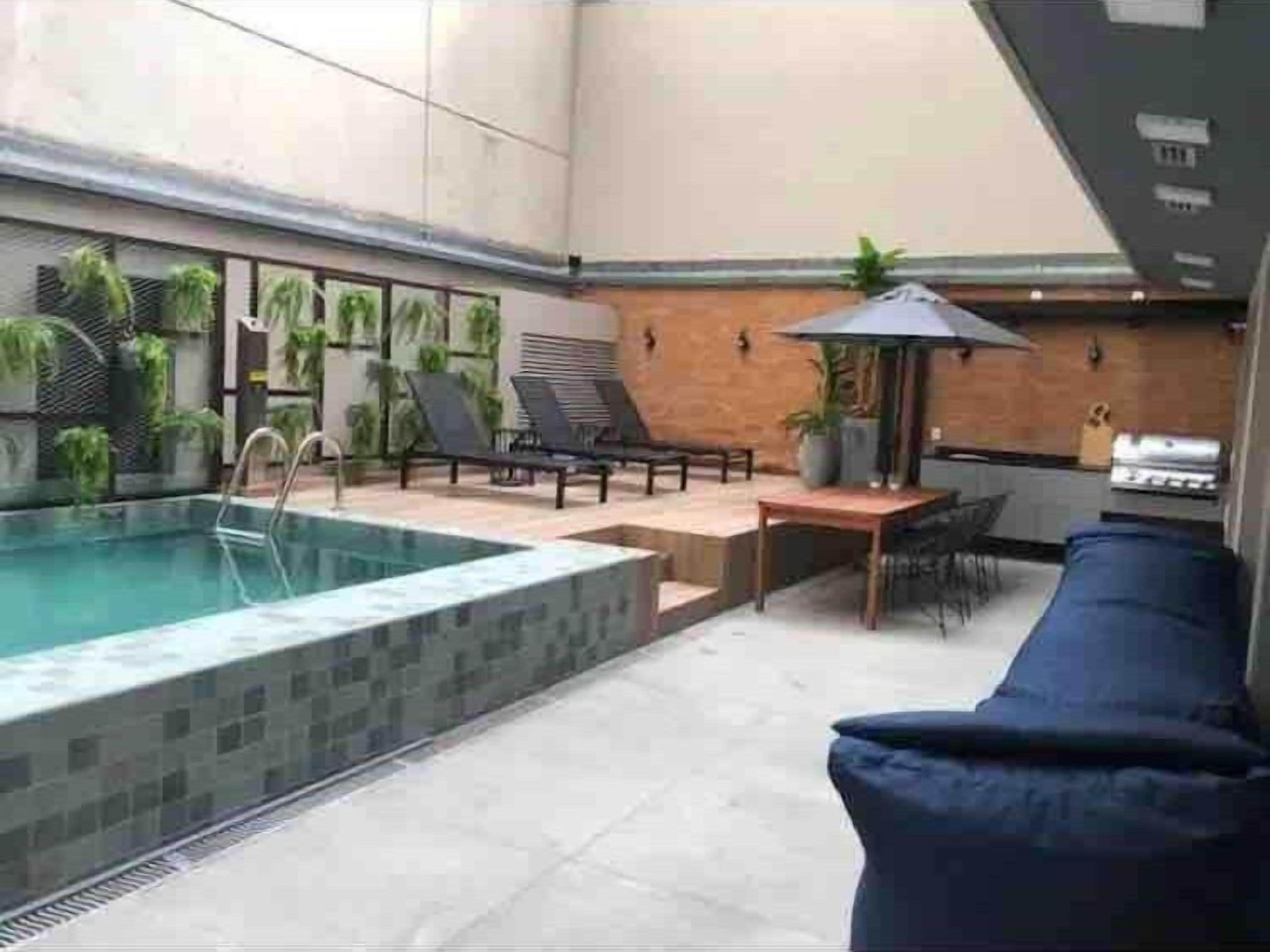 A pool area with a lounge chair, a table, and a grill.
