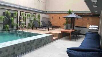 A pool area with a lounge chair, a table, and a grill.