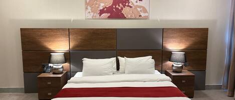 Quarto de hotel com uma cama grande, duas mesas de cabeceira com abajures, cabeceira com design de painel de madeira e uma obra de arte pendurada na parede.