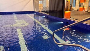 An indoor swimming pool with clear water, a metal ladder, and a modern interior design. - Garden Hotel (Jabriya)