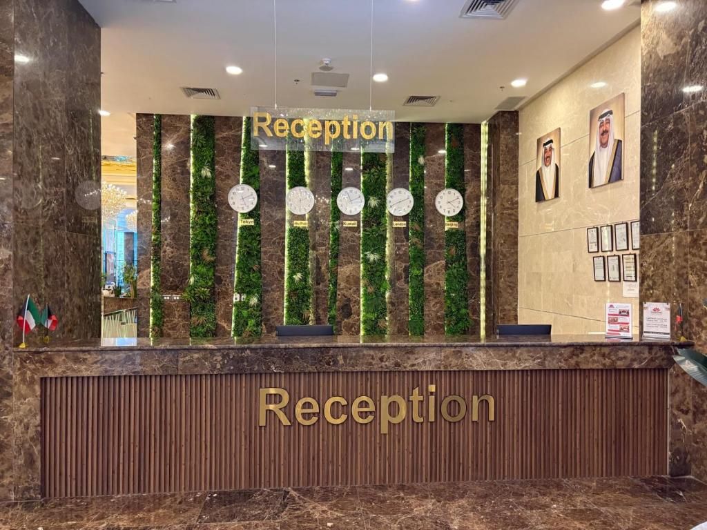 A reception desk with a 'Reception' sign above it, flanked by vertical green plant panels and clocks.